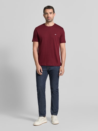Mannelijk model draagt Regular Fit t-shirt van puur katoen van GANT in bordeaux, gecombineerd met jeans, full body vooraanzicht.
