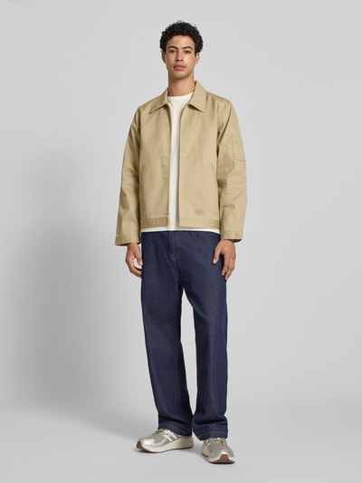 Männermodel trägt Jacke mit Reißverschluss Modell 'UNLINED EISENHOWER' von Dickies im Material-Mix mit Baumwoll-Anteil, Regular-Fit, Eingrifftaschen, Label-Detail, beige, glatte Textur, Ganzkörperansicht von vorne. Rückenlänge 67 cm, Schulterbreite 39 cm, Brustweite 53 cm, Ärmellänge 66 cm bei Größe M.