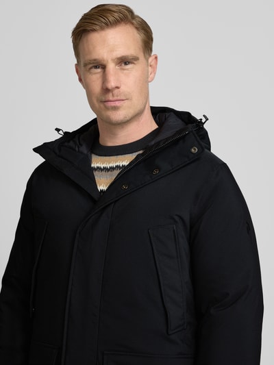 Männermodel draagt Parka met capuchon en klepzakken van PEAK PERFORMANCE, regular fit, zwarte stof, detailopname bovenlichaam. Ruglengte maat M: 87 cm, schouderbreedte: 47 cm, borstwijdte: 59 cm, mouwlengte: 73 cm.