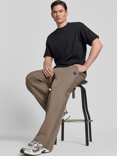 Männermodel trägt Comfort Fit Sweatpants aus Baumwoll-Mix Modell 'DROSPANT' von HUGO in Beige mit Lochstick-Einsatz, Ganzkörperansicht von vorne.