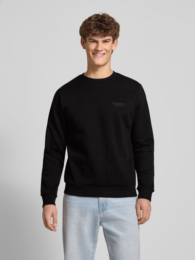 Männermodel trägt Sweatshirt mit Label-Print von JACK & JONES, Baumwoll-Mix, lockerer Schnitt, gerippte Abschlüsse, Rundhalsausschnitt, schwarze Farbe, Ganzkörperansicht von vorne.