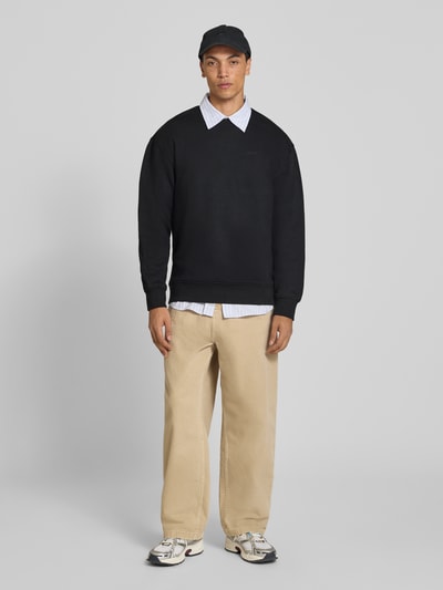 Männermodel trägt schwarzes Relaxed Fit Sweatshirt aus Baumwoll-Mix von Levi's®, beige Hose, neutrale Farbtöne, Ganzkörperansicht von vorne.