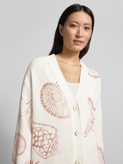 Modelka kobieca nosi Cardigan mit V-Ausschnitt im Allover-Look od Marc Cain, kremowo-biały, bawełniany miks, krój relaxed fit, z wzorem muszli i rozgwiazd, zapięcie na guziki, długość tyłu w rozmiarze 36: 70 cm, długość rękawa w rozmiarze 36: 56 cm, zbliżenie na górną część ciała
