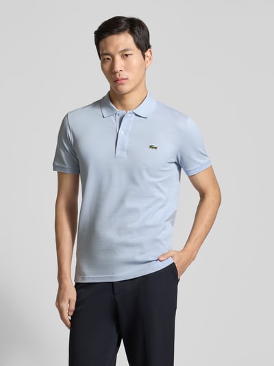 Männermodel trägt ein Slim Fit Poloshirt aus reiner Baumwolle von Lacoste in Hellblau mit Logo-Stitching, Piqué-Struktur, Ganzkörperansicht von vorne.