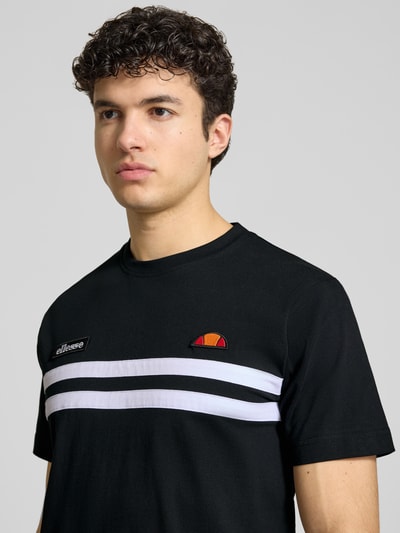 Männermodel trägt schwarzes Herren T-Shirt mit weißen Streifen, Label-Stitchings, Rundhalsausschnitt, Modell 'VENIRE' von Ellesse, Reine Baumwolle, Regular-Fit, Nahaufnahme Oberkörper.