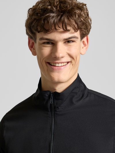 Männermodel trägt Regular Fit Jacke mit Stehkragen Modell 'Hefi' von Blend, czarna bawełna, zamek błyskawiczny, wpuszczane kieszenie, elastische wykończenia, Nahaufnahme Oberkörper. Długość tyłu w rozmiarze M: 71 cm, szerokość ramion: 46 cm, szerokość w rozmiarze M: 48 cm, długość rękawa: 25 cm.
