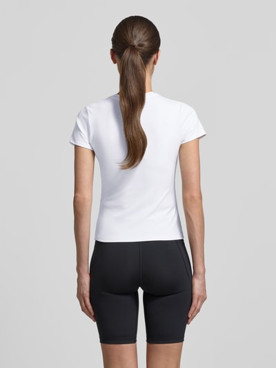 Modelka kobieca nosi T-Shirt mit Rundhalsausschnitt und Logo von Under Armour, biały materiał z elastyczną domieszką, krój slim fit, okrągły dekolt, logo, długość pleców w rozmiarze S: 49 cm, widok całej sylwetki od tyłu.