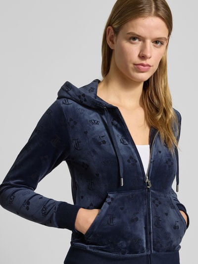 Kobiece model nosi bluzę rozpinaną model 'MONO MADISON' od Juicy Couture, mieszanka materiałów z dodatkiem streczu, krój slim fit, kaptur z tunelem, zamek błyskawiczny, kieszeń kangurka, ciemnoniebieska, wzór z logo, aksamitna faktura. Ujęcie: z przodu, górna część ciała.