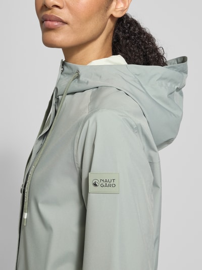 Frauenmodel trägt Jacke mit Ärmelriegeln von NAUTGÅRD in Hellgrau, Kapuze mit Tunnelzug, Reißverschlusstaschen, Nahaufnahme Oberkörper.