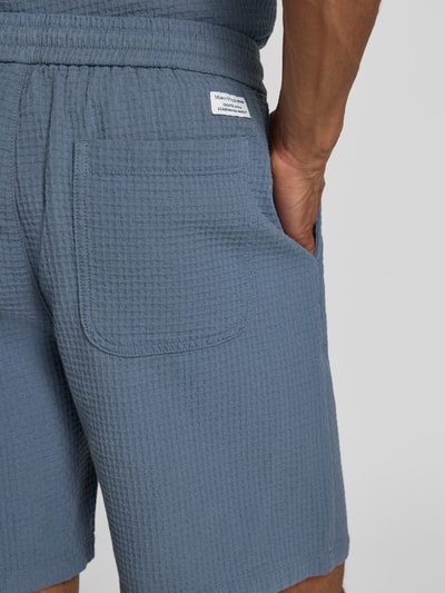 Männermodel trägt Regular Fit Sweatshorts aus reiner Baumwolle von Marc O'Polo Denim in Blau, Piqué-Struktur, Label Patch, Nahaufnahme Gesäßtasche.