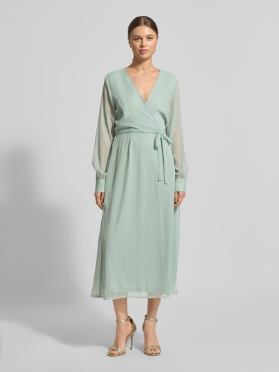 Frauenmodel trägt Midikleid mit Taillenband Modell 'FALIA' von Vila in Hellgrün, Wickel-Optik, V-Ausschnitt, semitransparente Optik, langärmlig, blickdichter Unterrock, taillierte Passform, Ganzkörperansicht von vorne.