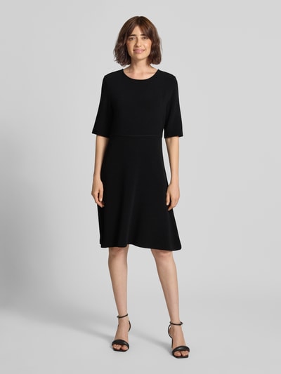 Frauenmodel trägt Minikleid aus Viskose-Mix mit Rundhalsausschnitt von Emporio Armani in Schwarz, taillierte Passform, Ganzkörperansicht von vorne.