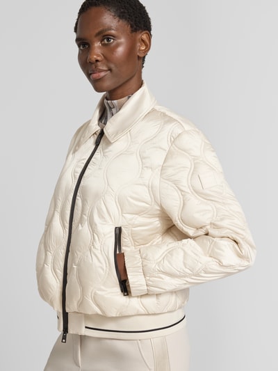 Frauenmodel trägt Steppjacke mit Umlegekragen und Reißverschlusstaschen von Marc Cain in hellem Beige mit sichtbarer Steppstruktur, Regular Fit, Reißverschluss und Reißverschlusstaschen, Ganzkörperansicht von vorne. Rückenlänge, Schulterbreite, Brustweite und Ärmellänge gemäß Größe 36.