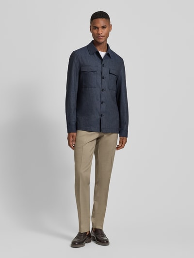 Männermodel trägt beige pantalon aus mix van scheerwol en elastaan Modell 'Sendrik' von Carl Gross mit persplooien en achterzakken, regular fit, bandwijdte maat 50: 40 cm, binnenbeenlengte maat 50: 85 cm, ganzkörperansicht von vorne.
