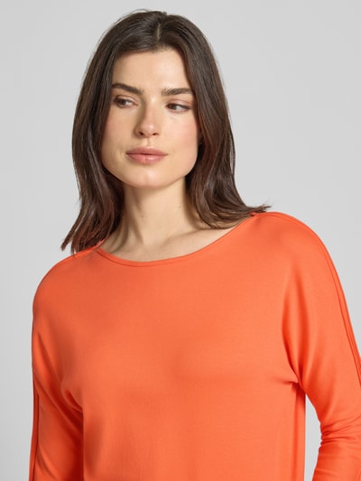 Modelka kobieca nosi T-Shirt mit 3/4-Arm od Marc Cain w kolorze pomarańczowym, bawełna z elastanem, prosty krój, dekolt łódka, z kieszenią i aplikacją z logo, długość tyłu w rozmiarze 36: 49 cm, zbliżenie na górną część ciała.