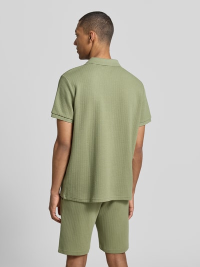 Męski model nosi Regular Fit Strick-Poloshirt mit V-Ausschnitt von MCNEAL, mieszanka bawełny z dodatkiem streczu, krój regular fit, dekolt w serek, długość tyłu w rozmiarze M: 70 cm, jasna zieleń, widoczne fakturowanie dzianiny, całkowity widok z tyłu.
