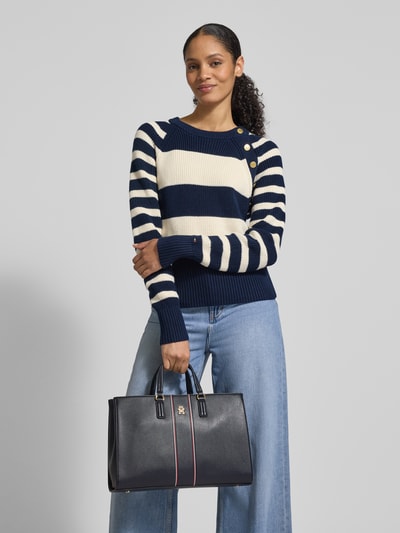 Modelka kobieca prezentuje Henkeltasche in Leder-Optik od Tommy Hilfiger, granatowy kolor, logo z metalu, pasek na ramię, widok całej sylwetki z przodu