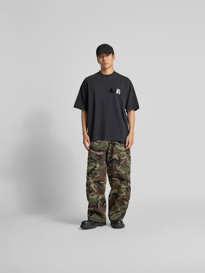Männermodel trägt Relaxed Fit Cargohose aus Baumwolle von VETEMENTS mit Camouflage, Eingrifftaschen, Cargotaschen, Ganzkörperansicht von vorne.