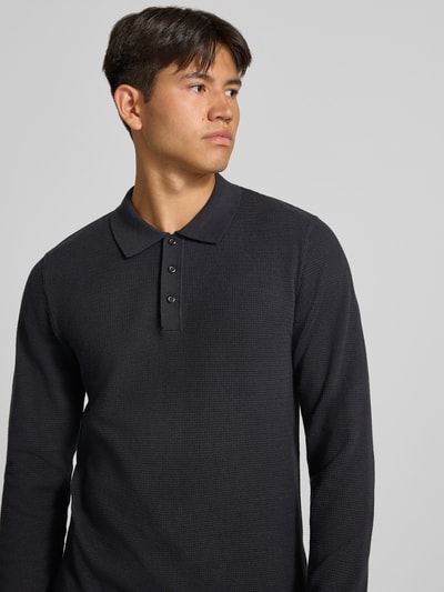 Männermodel trägt Slim Fit Poloshirt mit Label-Detail Modell 'AUSTIN' von JACK & JONES, dunkler Baumwoll-Mix, Struktur-Muster, Nahaufnahme Oberkörper.