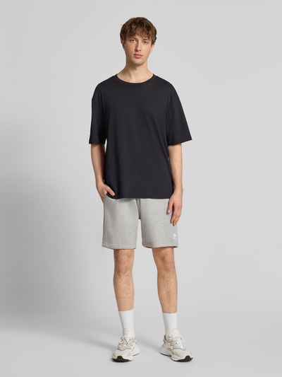 Männermodel trägt Regular Fit Sweatpants mit Logo-Stitching von adidas Originals im Baumwoll-Mix, hellgrau, Knielänge, Ganzkörperansicht von vorne.