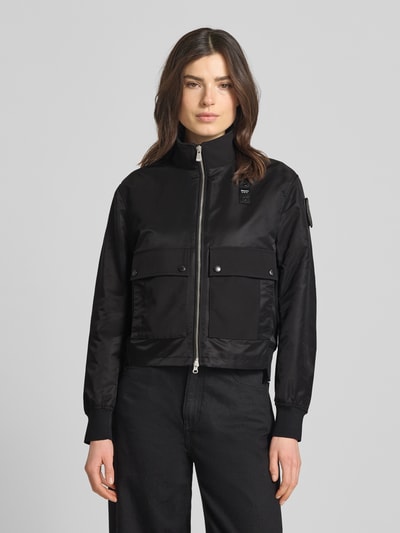 Vrouwenmodel draagt Jacke mit Stehkragen Modell 'CARNY' van Blauer Usa, rechte fit, zwart, gladde textuur, opgestikte zakken, tweewegrits, elastische mouwboorden, detailopname bovenlichaam.