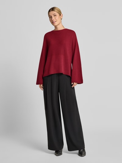 Frauenmodel trägt Oversized Pullover aus reiner Baumwolle in Strick-Optik von Emporio Armani, dunkelrot, kombiniert mit schwarzer Hose, elastische Abschlüsse und überschnittene Schultern, Ganzkörperansicht von vorne.