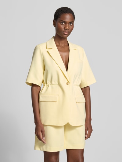 Modelka prezentuje żakiet Relaxed Fit Blazer mit Viskose-Anteil Model 'Likka' od YAS, elastyczna mieszanka materiałów z dodatkiem wiskozy, krój relaxed fit, Kołnierz z połami, rękaw o dł. 1/2, zapięcie na guzik, Kieszenie z patką, Długość tyłu w rozmiarze 36: 70 cm, pastelowy żółty, gładka faktura, widok całej sylwetki z przodu.
