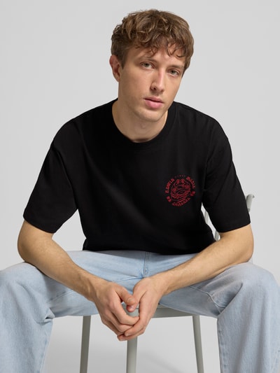 Männermodel trägt schwarzes T-Shirt aus reiner Baumwolle Modell 'MUSIC CHANNEL' von Edwin mit rotem Print, Nahaufnahme Oberkörper. Gerader Schnitt, Rundhalsausschnitt.