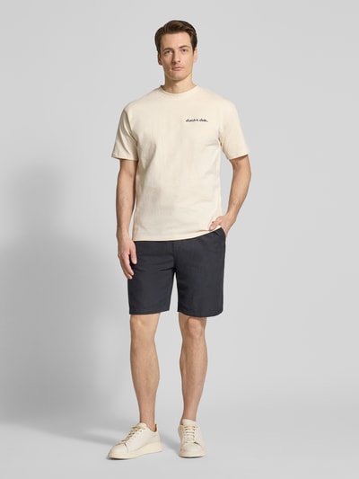 Männermodel trägt T-Shirt mit Label-Stitching von Scotch & Soda in Beige, Reine Baumwolle, Regular-Fit, Rundhalsausschnitt, Ganzkörperansicht von vorne.