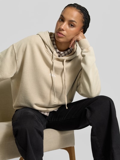 Frauenmodel trägt Oversized Hoodie aus reiner Baumwolle von Lala Berlin in Beige mit Kapuze, Tunnelzug und Label-Print, Nahaufnahme Oberkörper.