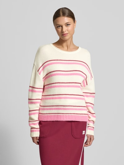 Modelka kobieca ma na sobie Regular Fit Pullover aus Alpaka-Mix mit Kaschmir-Anteil von Marc Cain, w kremowe i różowe paski, krój regular fit, okrągły dekolt, elastyczne wykończenia, dzianinowa faktura, długość tyłu w rozmiarze 36: 56 cm, długość rękawa: 51 cm, ujęcie całej sylwetki z przodu.