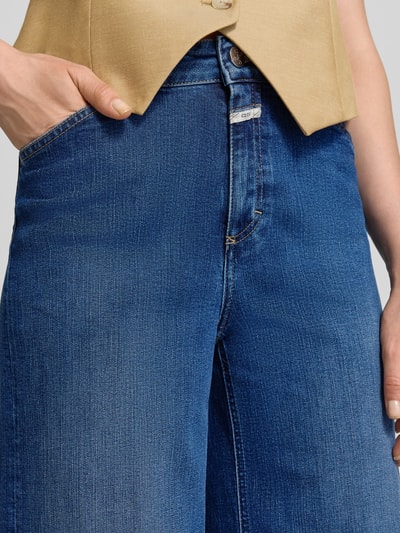 Frauenmodel trägt Wide Leg Jeans mit Label-Detail Modell 'WERA' von Closed in Mittelblau mit sichtbarer Textur, Nahaufnahme Hüfte, Baumwoll-Mix mit Stretch-Anteil, Eingrifftaschen, strukturierte Oberfläche.