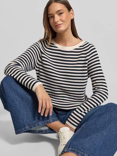 Frauenmodel trägt Regular Fit Pullover aus reiner Baumwolle von Tommy Hilfiger, cremefarben mit navyblauen Streifen, Rippstrick, Logo-Stitching, Rundhals, langarm, unifarbene Optik mit strukturierter Textur, Nahaufnahme Oberkörper.