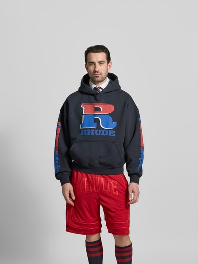 Männermodel trägt Oversized Hoodie aus Baumwolle von RHUDE in Dunkelblau mit Label-Prints, Känguru-Tasche, elastische Abschlüsse, Reine Baumwolle, Rückenlänge bei Größe M: 65 cm, Ganzkörperansicht von vorne.