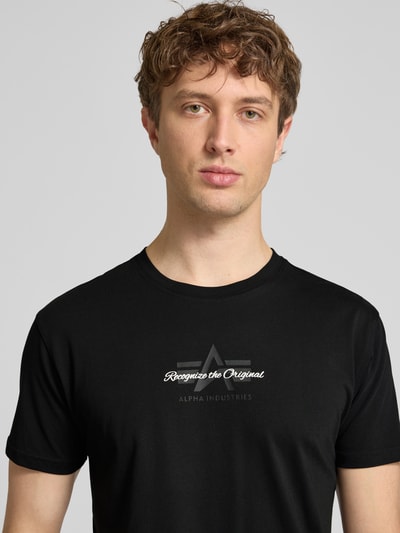 Mężczyzna nosi T-Shirt mit Label-Detail Modell 'Foam' von Alpha Industries, czarny, bawełna, krój regular fit, nadruk na piersi, ujęcie z przodu na górną część ciała
