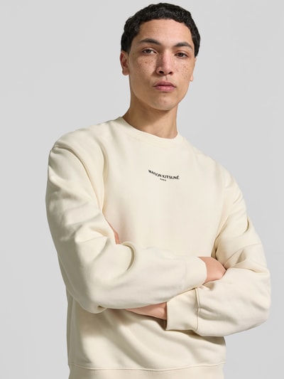 Männermodel trägt Hoodie aus Baumwoll-Mix von MAISON KITSUNÉ in Creme mit Rundhalsausschnitt und Label-Stitching, Nahaufnahme Oberkörper.