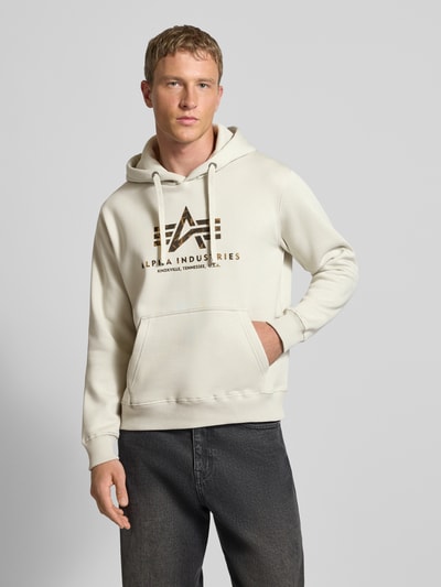 Männermodel trägt Hoodie mit Logo und Känguru-Tasche von Alpha Industries in Creme, Baumwoll-Mix, Regular Fit, Nahaufnahme Oberkörper.