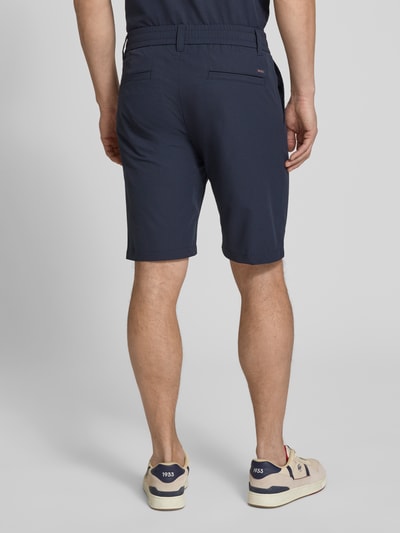Mężczyzna nosi Tapered Fit Bermuda mit Kordelzug Modell 'CHINO' von BOSS Orange w granatowym kolorze z fakturą crinkle, widok całej sylwetki z tyłu.