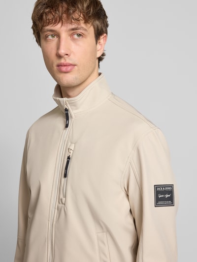 Männermodel trägt Regular Fit Bomberjacke mit Stehkragen Modell 'Parker' von Jack & Jones in Beige, Softshell, Nahaufnahme Oberkörper. Kontext: Herrenjacke mit Napoleontasche, Eingrifftaschen mit Druckknopfverschluss, elastische Abschlüsse, Maße bei Größe M: Rückenlänge 67 cm, Schulterbreite 43 cm, Brustweite 55 cm, Ärmellänge 65 cm.