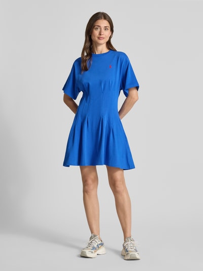 Frauenmodel trägt Leicht ausgestelltes Sweatkleid aus reiner Baumwolle von Polo Ralph Lauren, kolor melanż, krój lekko rozkloszowany, długość mini, okrągły dekolt, wyhaftowane logo, fałdy, rękaw krótki, wykończenie materiału: dzianina dresowa, materiał: bawełna, widok: całkowita sylwetka z przodu.