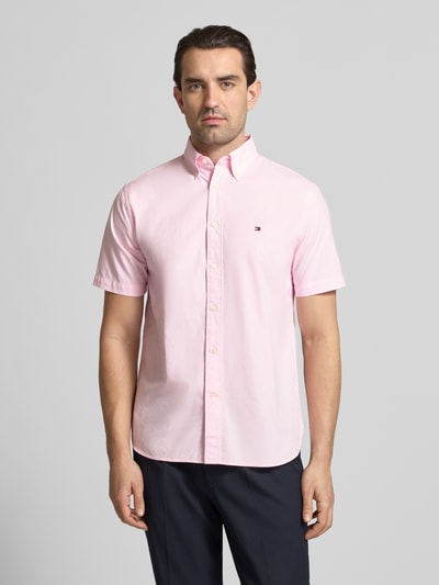 Männermodel trägt Regular Fit Freizeithemd aus reiner Baumwolle von Tommy Hilfiger in zartem Rosa mit Button-Down-Kragen, Optik: Allover-Muster, Mini-Hahnentritt, Logo-Stitching, Popeline, Kurzarm, Ganzkörperansicht von vorne.