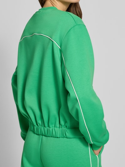 Frauenmodel trägt Regular Fit Jacke mit Viskose-Anteil Modell 'Kate' von ICHI in kräftigem Grün mit weißer Paspel, Elastischer-Material-Mix, elastische Ärmelabschlüsse und durchgehende Knopfleiste; Ganzkörperansicht Rückansicht.
