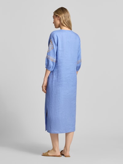 Frauenmodel trägt Tunikakleid aus Leinen mit Tunikakragen und Quasten von Emily Van den Bergh in Hellblau mit Motiv-Stitching, Loose Fit, Midikleid, natürliche Leinenstruktur, Rückenansicht Ganzkörperansicht.