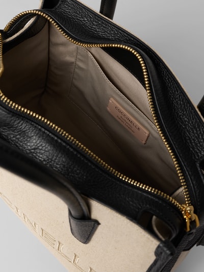 Produktfoto, Handtasche mit Label-Stitching von Coccinelle, Hauptfach mit Reißverschluss, Tragehenkel, Schulterriemen, Breite 27 cm, Länge 20 cm, Tiefe 13 cm, Schulterriemen 105 cm, beige-schwarze Farbgebung, strukturierte Oberfläche, sichtbare Stitching-Details, Innenansicht des Hauptfachs.