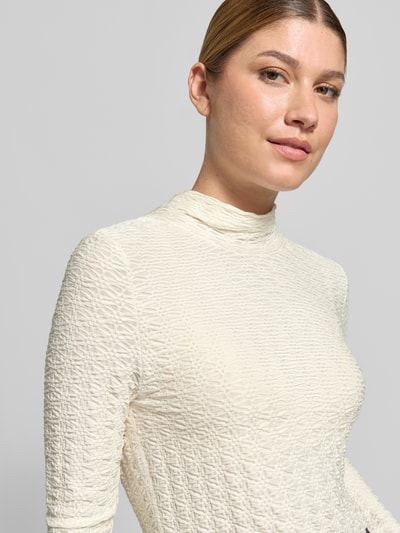 Frauenmodel trägt Skinny Fit Longsleeve aus Viskose-Mix von Marc Cain in Creme mit Strukturmuster und Stehkragen, Nahaufnahme Oberkörper.