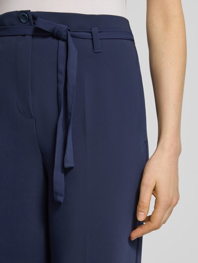 Frauenmodel trägt Hose mit Bindegürtel und Bügelfalten von More & More in Dunkelblau mit Gesäßtaschen, Nahaufnahme Oberkörper. Bundweite bei Größe 36: 35 cm, Innenbeinlänge: 78 cm, Regular-Fit. Stoff mit glatter Textur.