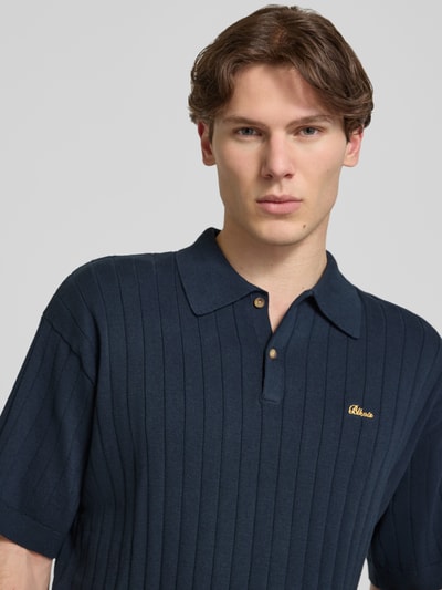 Männermodel trägt Regular Fit Strick-Poloshirt mit Label-Stitching von BLKVIS, Reine Baumwolle, Ripp-Optik, Knopfleiste, Nahaufnahme Oberkörper.