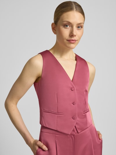 Frauenmodel trägt Weste aus Satin mit V-Ausschnitt von Jake*s Cocktail in Pink mit Knopfleiste, Paspeltaschen, Slim-Fit, Nahaufnahme Oberkörper.