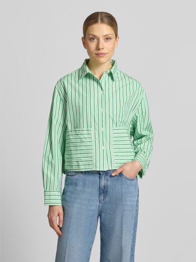 Vrouwenmodel draagt Loose Fit Langarmbluse aus reiner Baumwolle van s.Oliver RED LABEL in effen kleuren gestreept popeline, groen en wit, cropped lengte met overhemdkraag, V-hals, knoopsluiting, opgestikte zakken, rugpas met cacharelplooi, asymmetrische rompzoom, puur katoen. Ganzkörperansicht van voren.