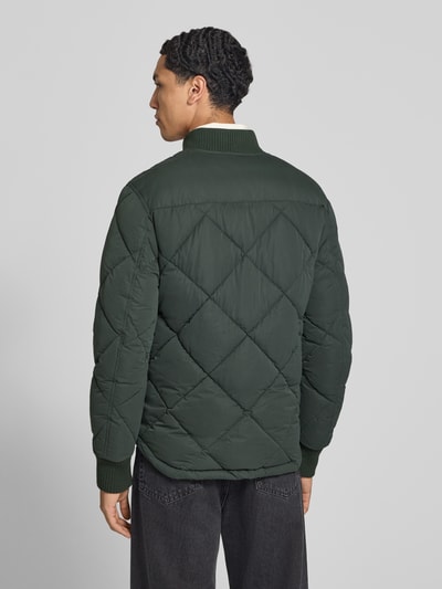 Männermodel trägt Regular Fit Steppjacke mit opstaande kraag van Superdry, donkergroen met Stiksels, Steekzakken, elastische mouwboorden, ritssluiting, Ruglengte maat M 69 cm, schouderbreedte 46 cm, borstwijdte 58 cm, mouwlengte 59 cm, doorgestikte textuur, Ganzkörperansicht Rückansicht